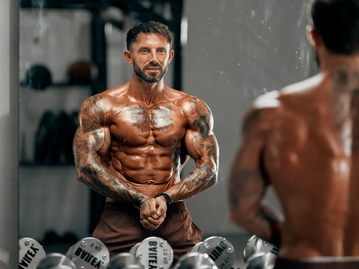 Posing in front of the gym mirror above a rack of dumbbells